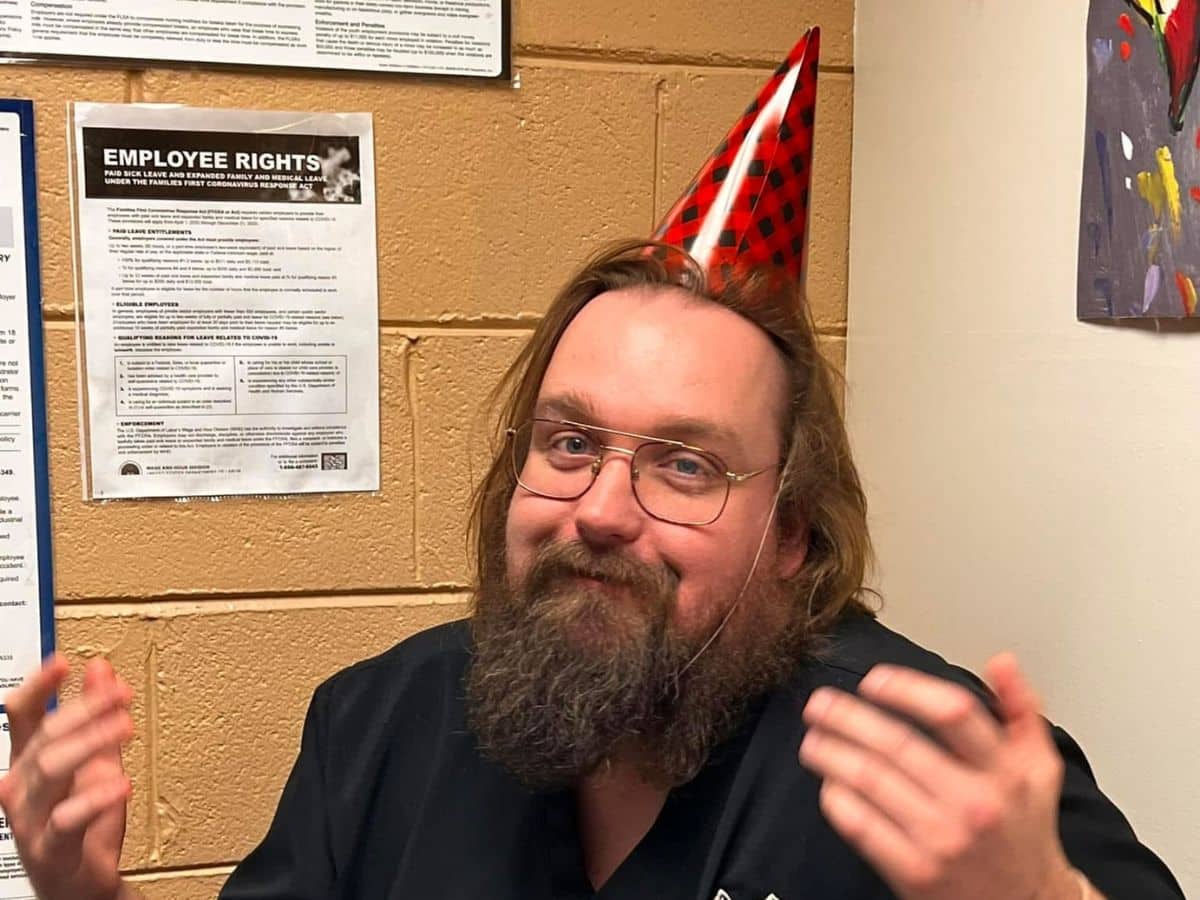 A bearded man wearing a colorful birthday hat